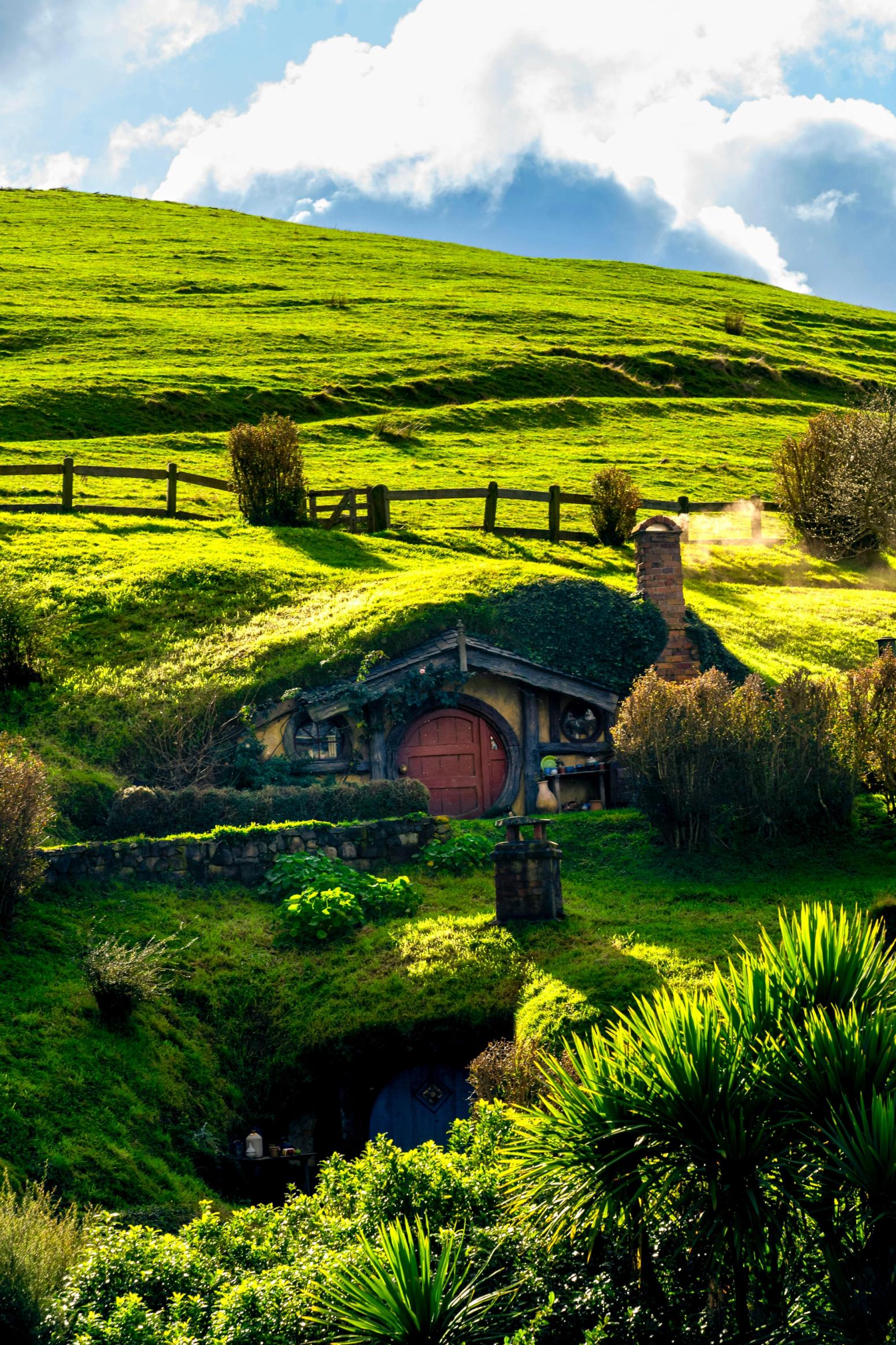 Hobbit-Haus in grüner Hügellandschaft mit runder Tür und Schornstein