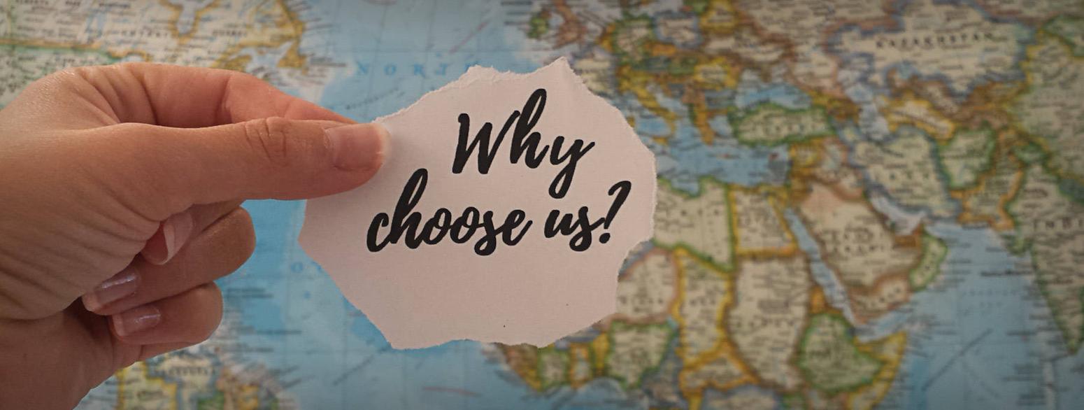 Ein Stück Papier mit der Aufschrift "why choose us?" wird vor eine Weltkarte gehalten. 