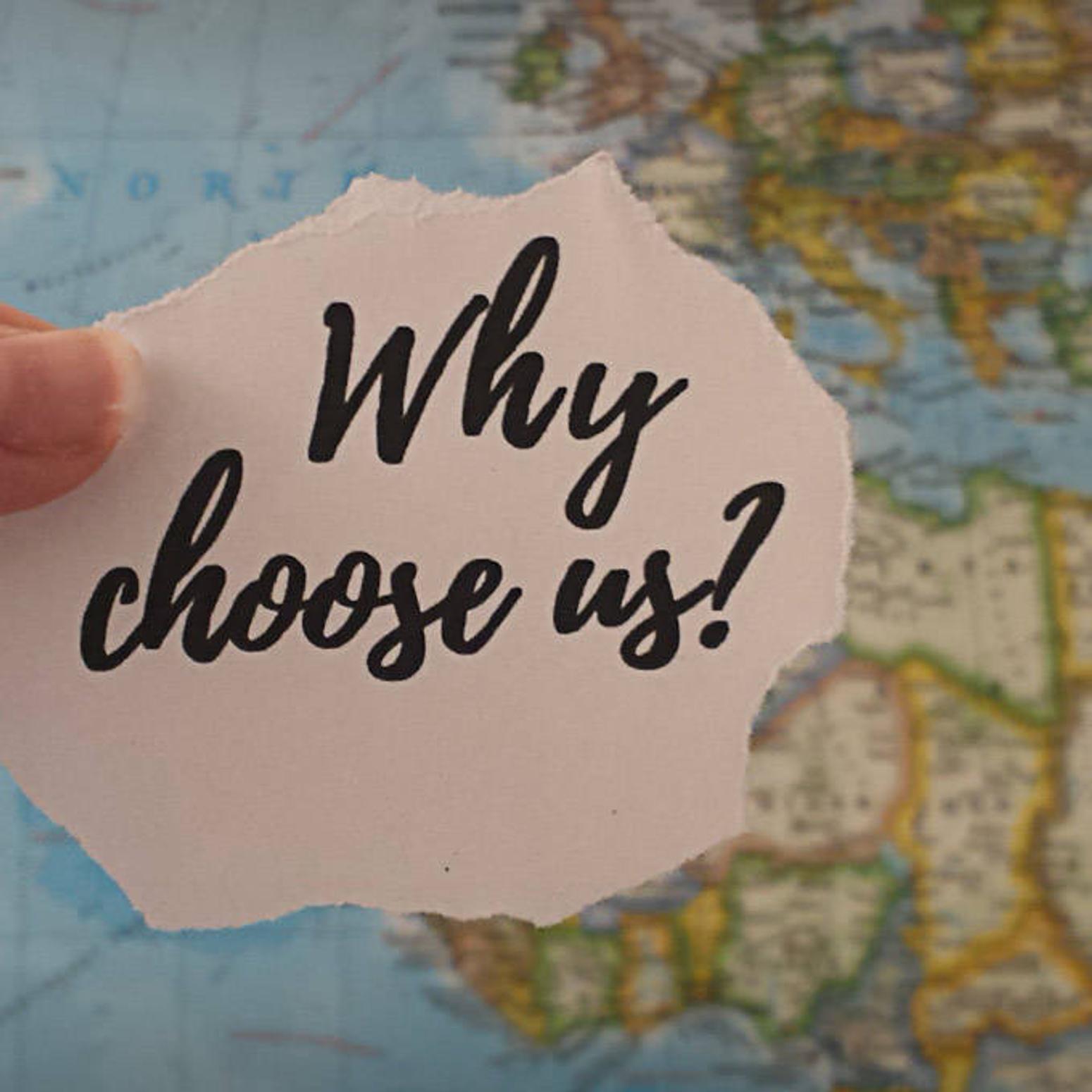 Ein Stück Papier mit der Aufschrift "why choose us?" wird vor eine Weltkarte gehalten. 