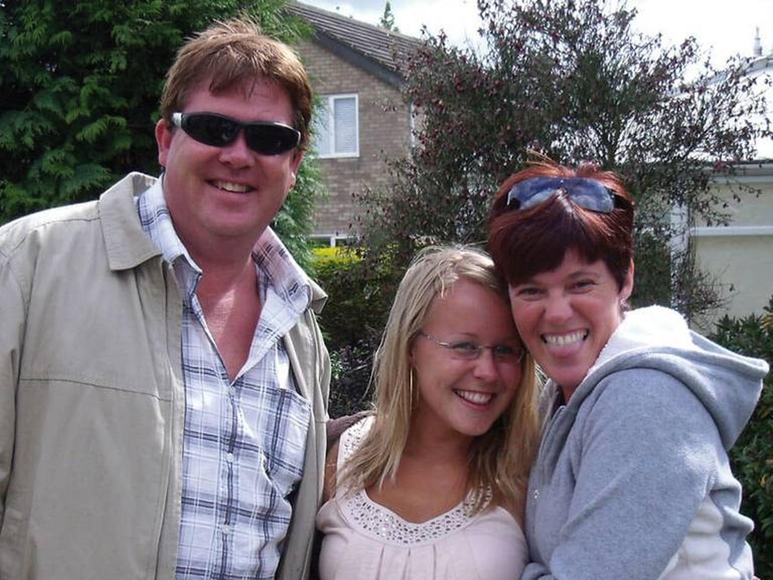 Das Bild zeigt einen Mann und zwei Frauen die sich in den armen halten und in die Kamera lächeln 