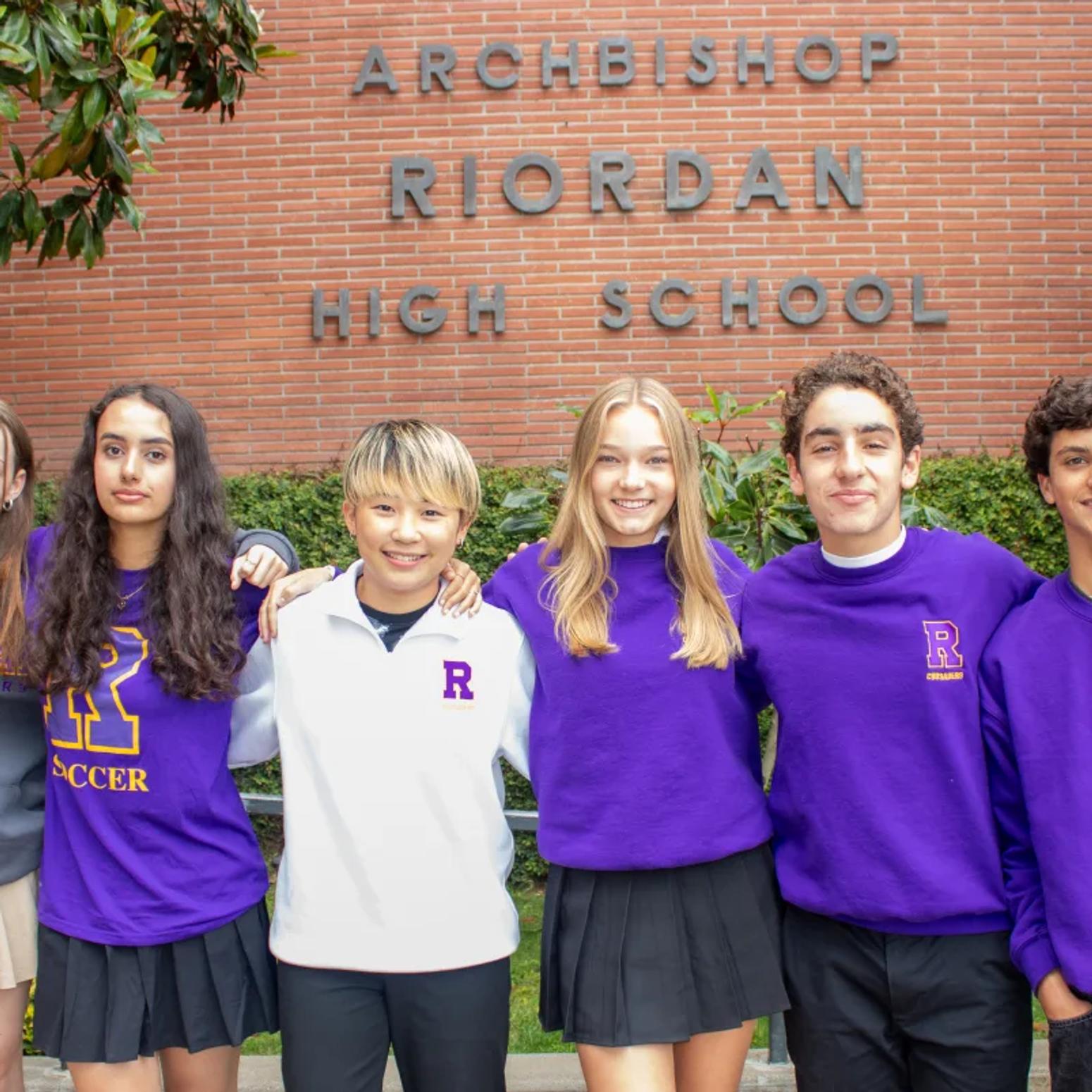 Sechs Jugendliche in Schuluniformen stehen lächelnd vor der Archbishop Riordan High School.