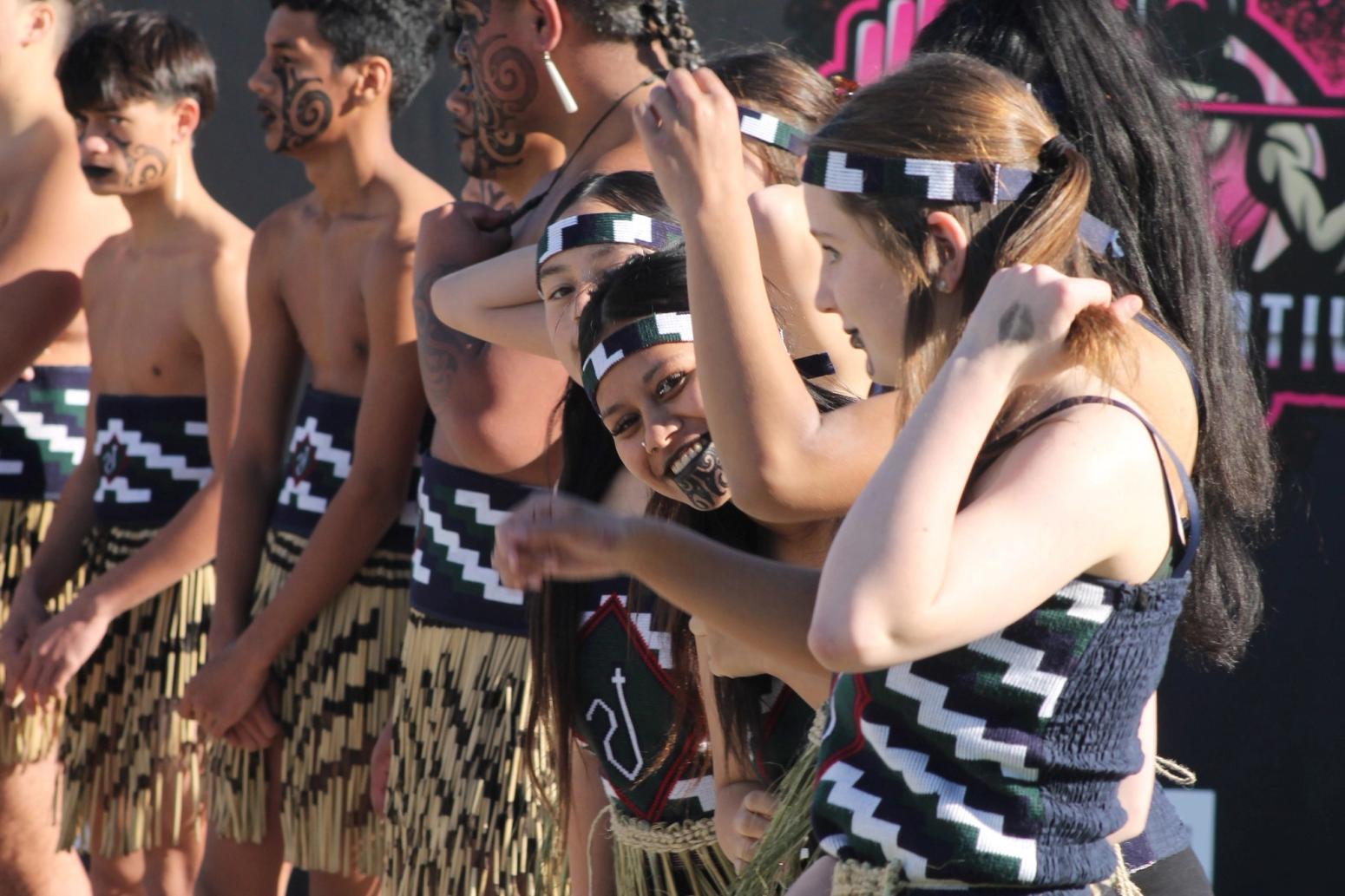 Schülerinnen und Schüler in traditioneller Kleidung mit Gesichtsbemalung bereiten sich auf eine kulturelle Aufführung in Neuseeland vor.