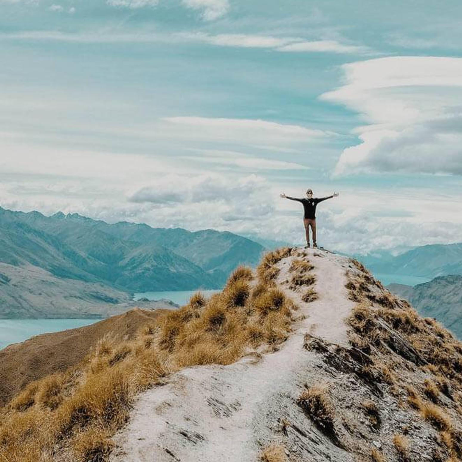 Ein Mann steht an der spitze von einem Berg und breitet seine Arme aus