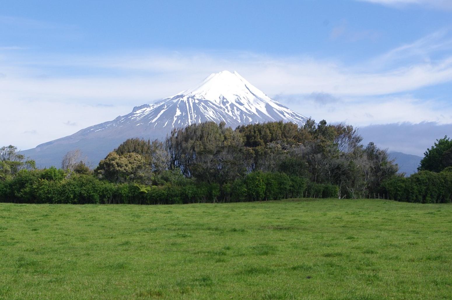 Mount Taranaki mit Schnee bedeckt vor blauem Himmel und mit grüner Wiese
