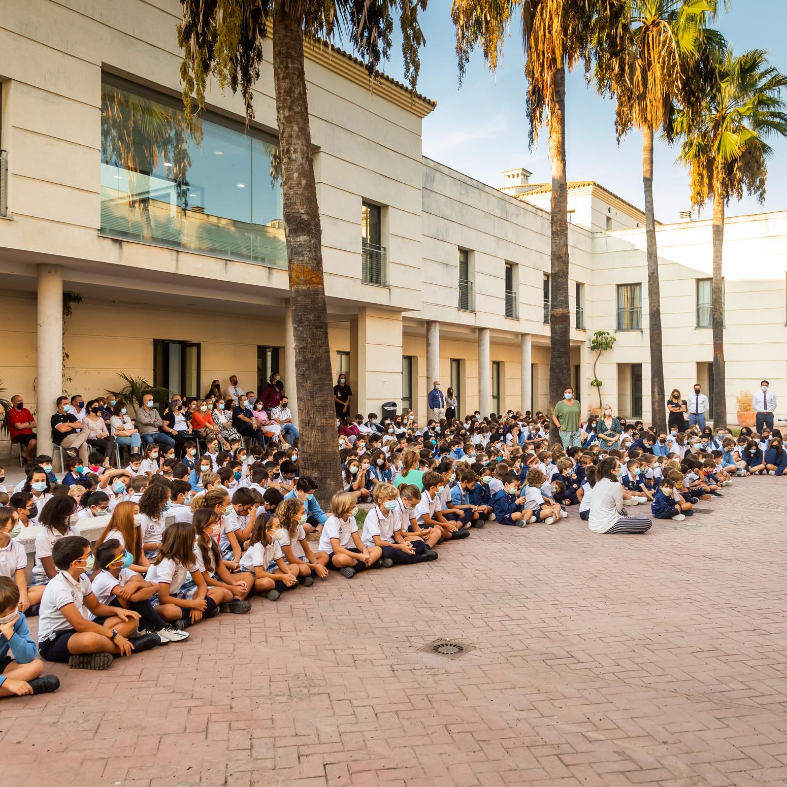 Sage College Jerez Spanien Schüler:innen hören dem Rektor bei einer Rede zu und sitzen draußen auf dem Boden