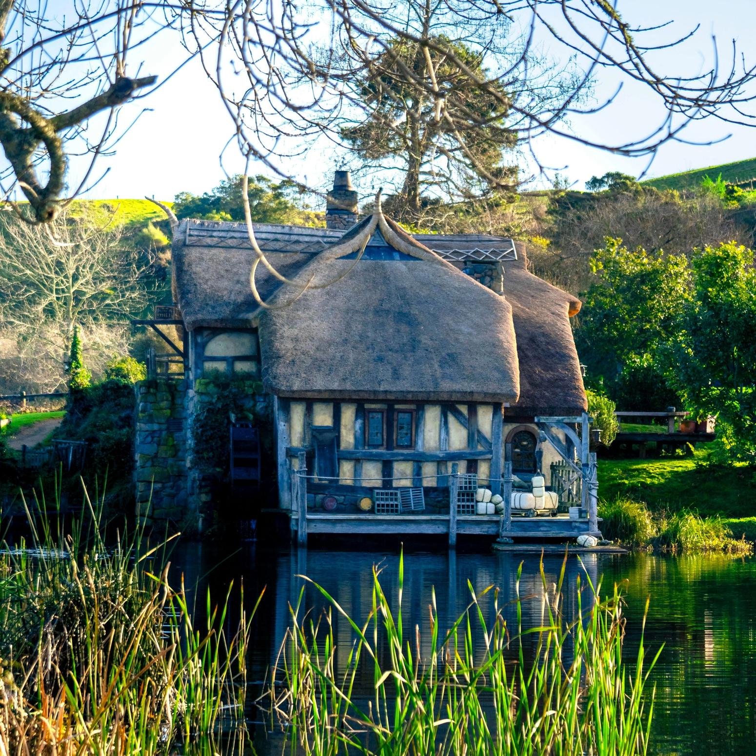 Reetgedecktes Haus am Wasser in Hobbiton, umgeben von Bäumen und Schilf