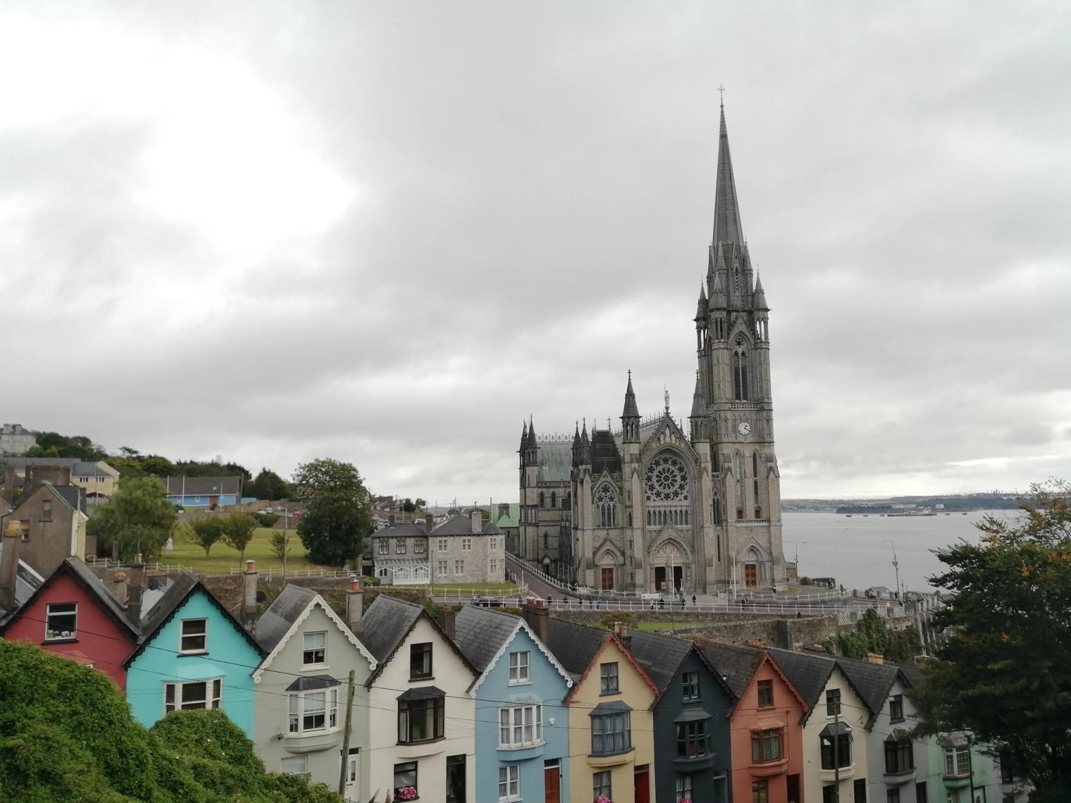 Küstenpanorama in Irland mit bunten Häusern im Vordergrund und Kathedrale im Hintergrund