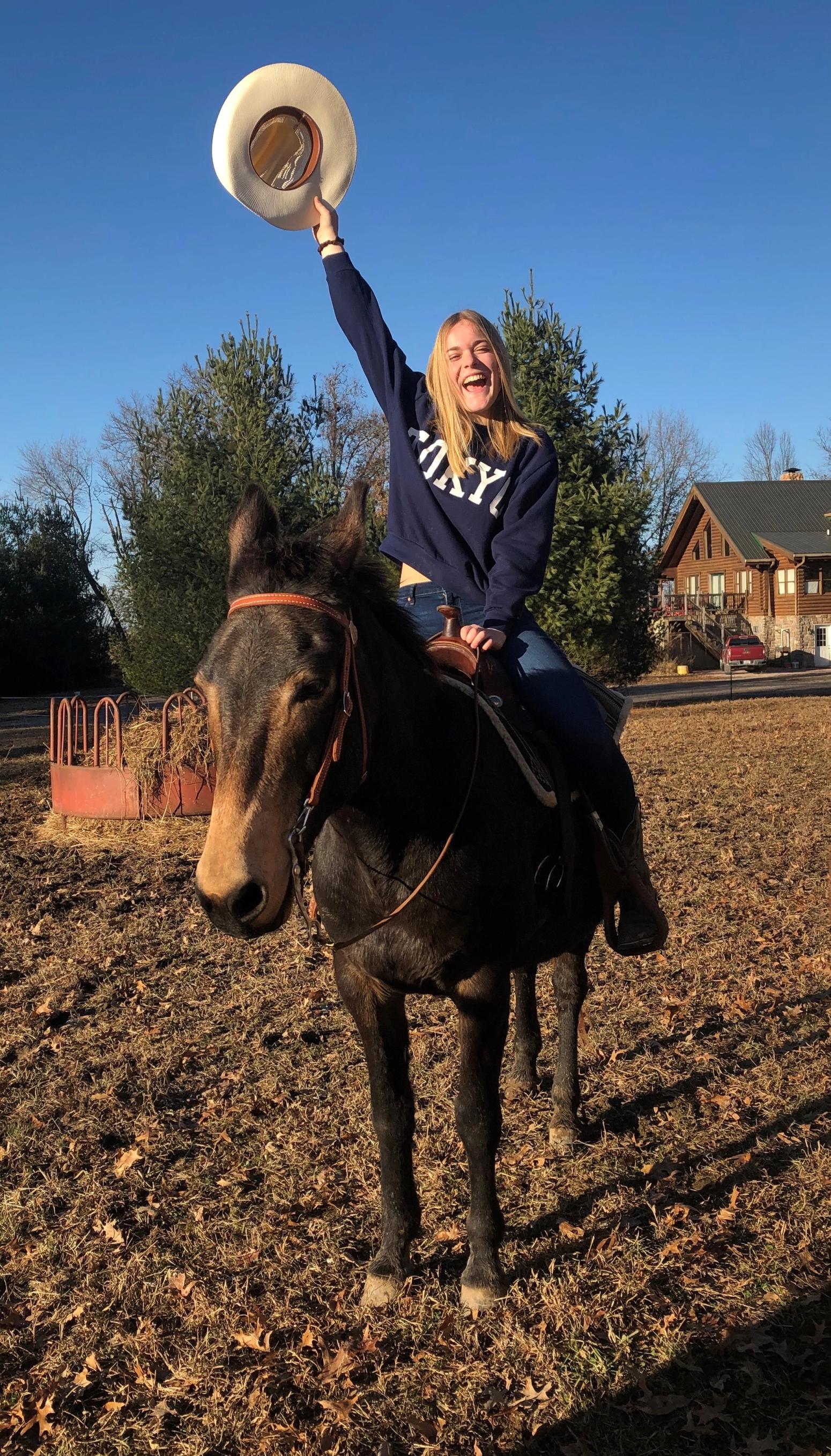 Schülerin reitet lachend auf einem Pferd und schwenkt einen Hut – Moment aus einem Auslandsaufenthalt