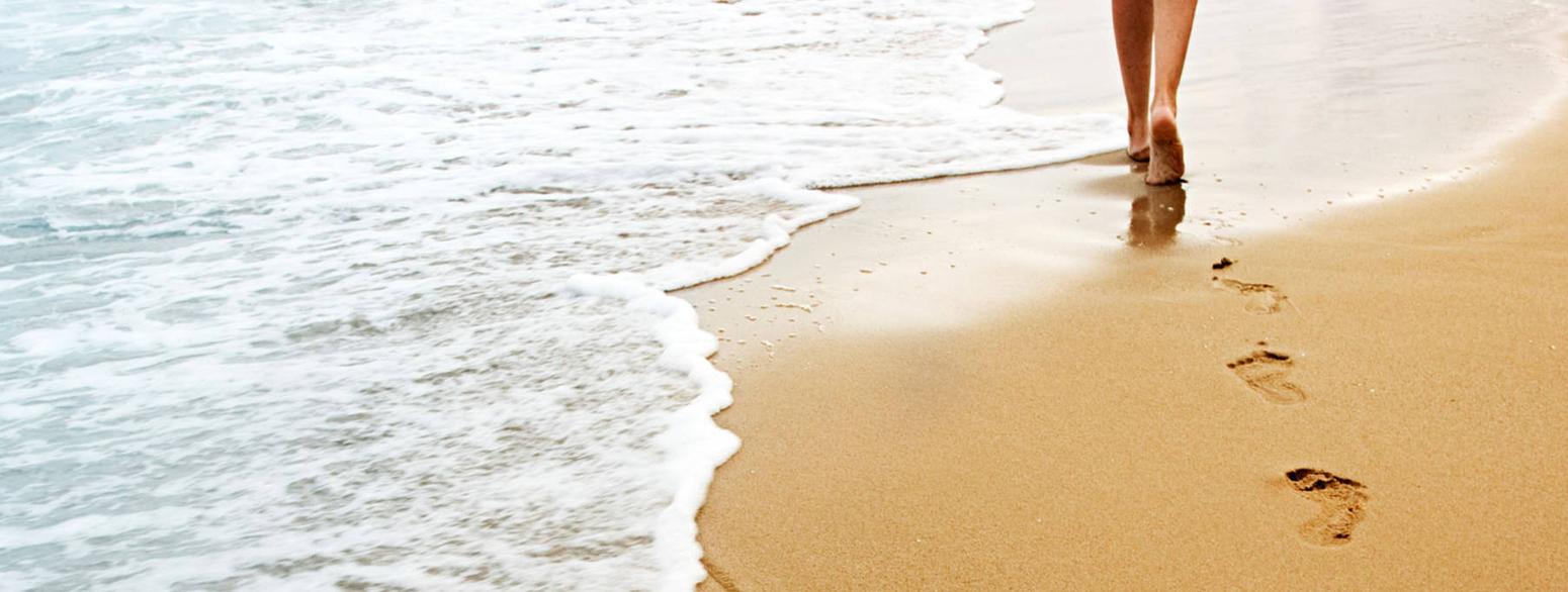 Eine Person läuft am Strand und hinterlässt Fußspuren um Sand 