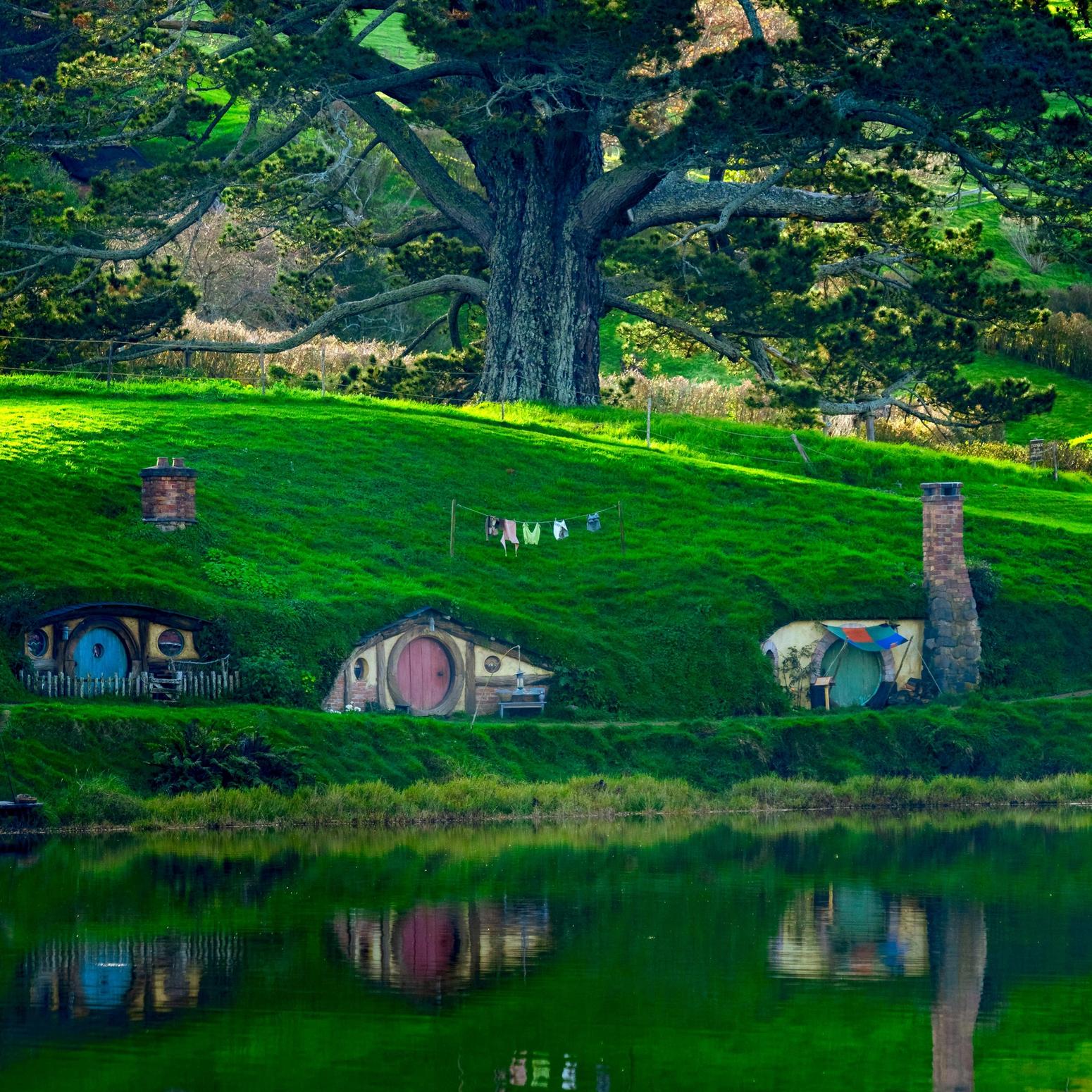 Hobbit-Häuser mit runden Türen in einer grünen Hügellandschaft am Seeufer