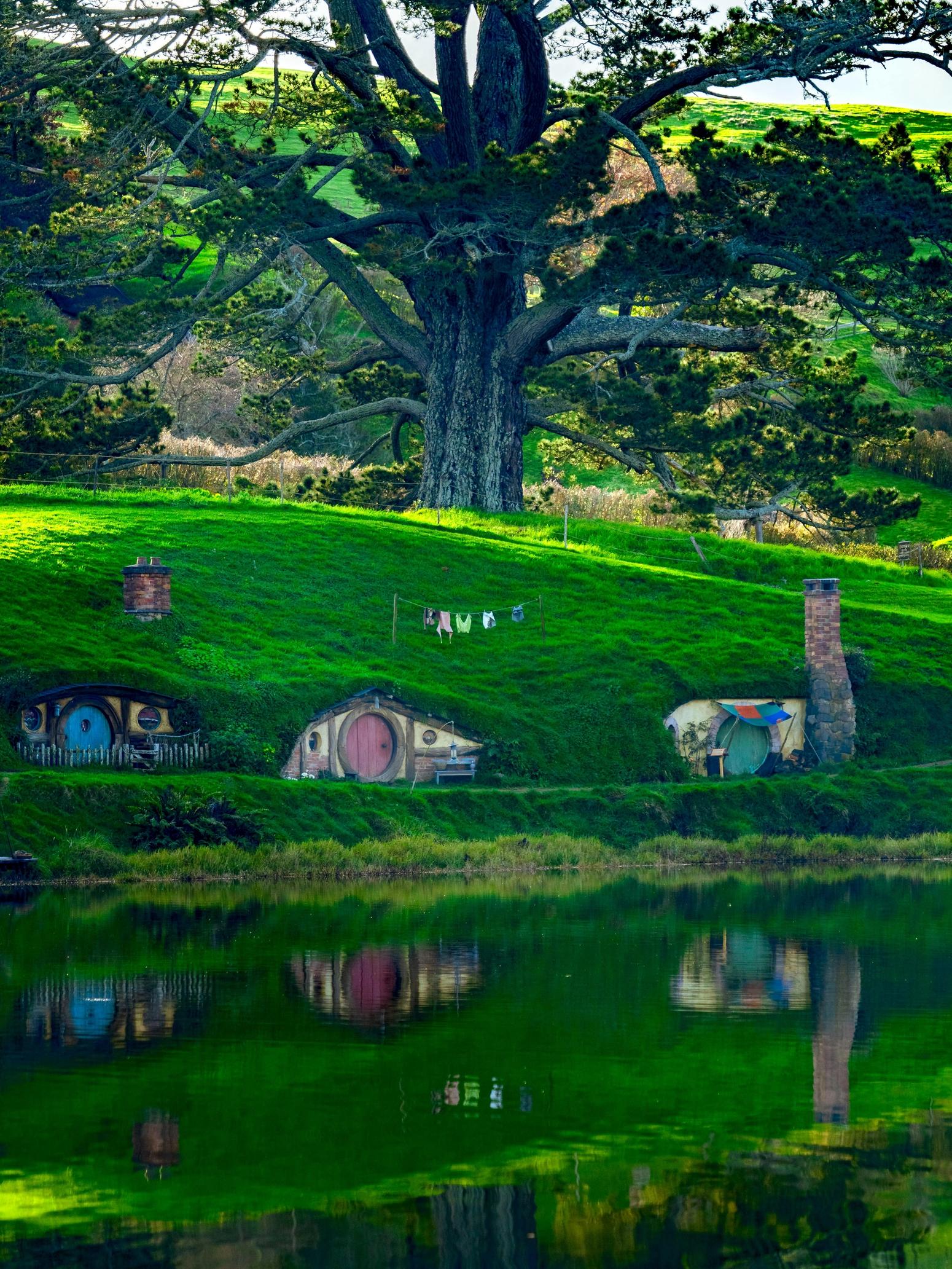 Hobbit-Häuser mit runden Türen in einer grünen Hügellandschaft am Seeufer