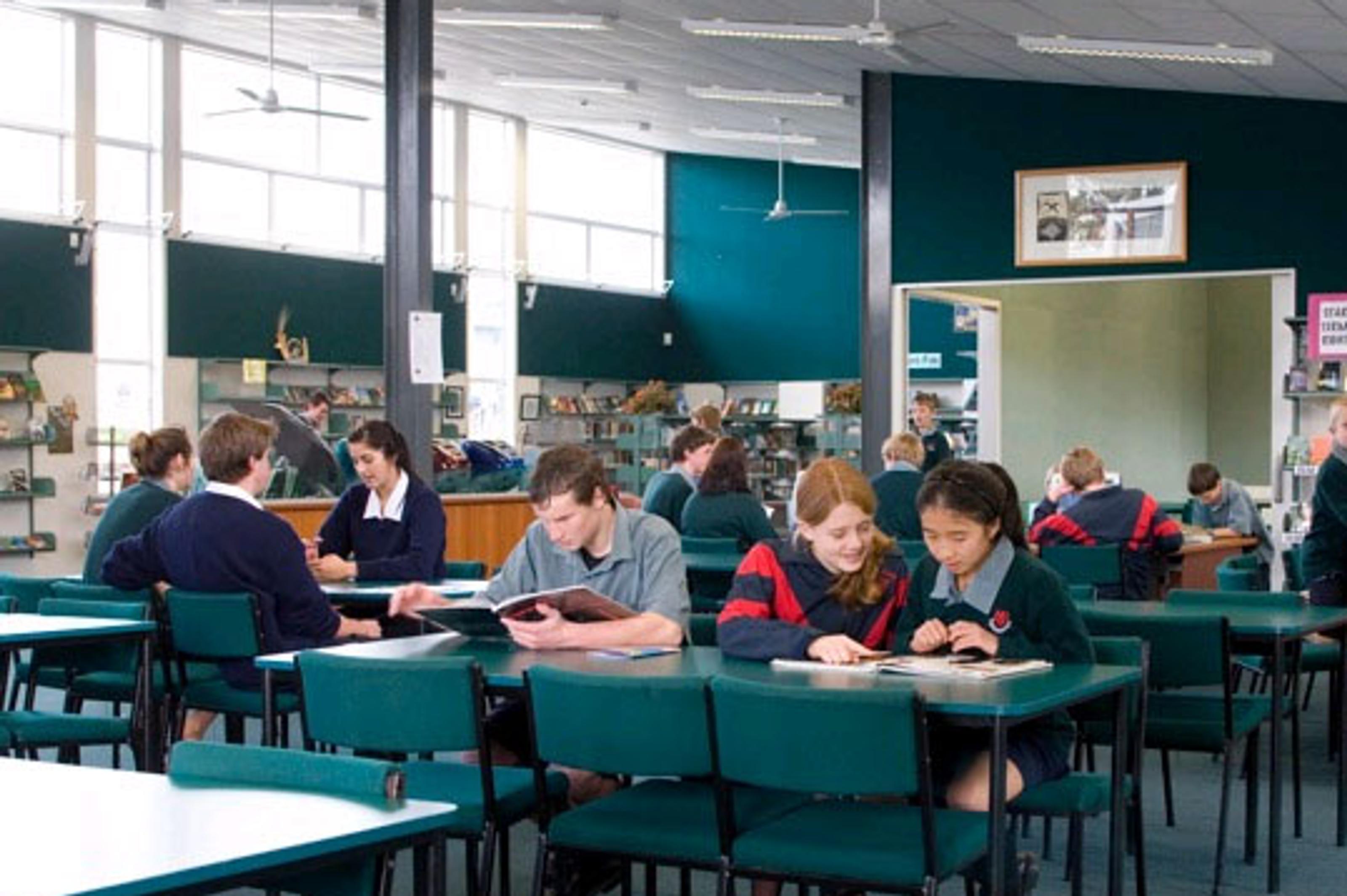 Schüler:innen lernen an Tischen im Schulgebäude