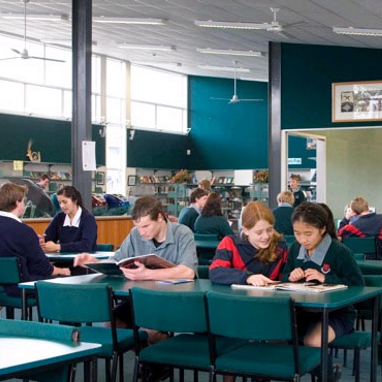 Schüler:innen lernen an Tischen im Schulgebäude