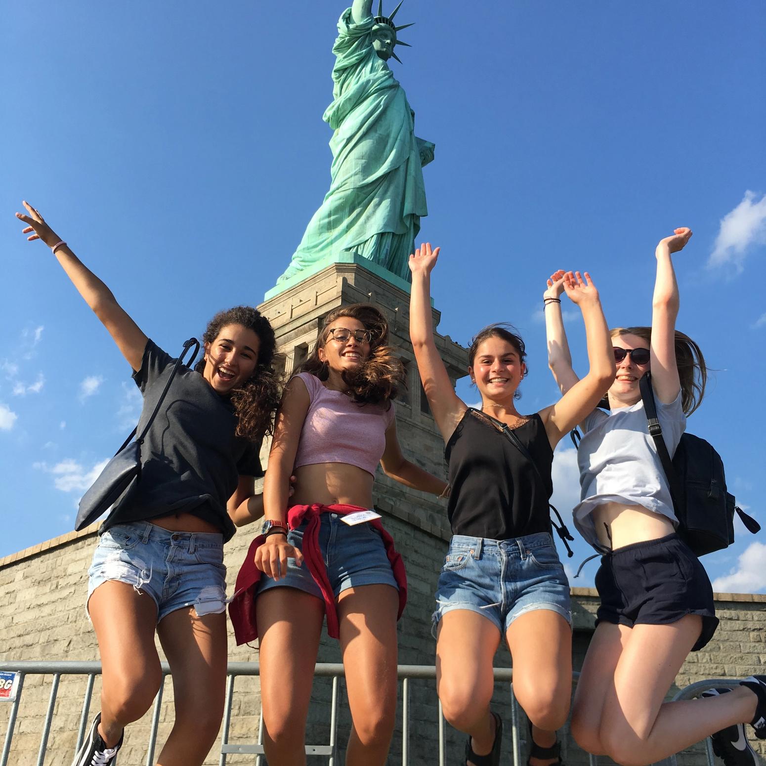 Vier junge Frauen springe vor der Freiheitsstatue in die Luft
