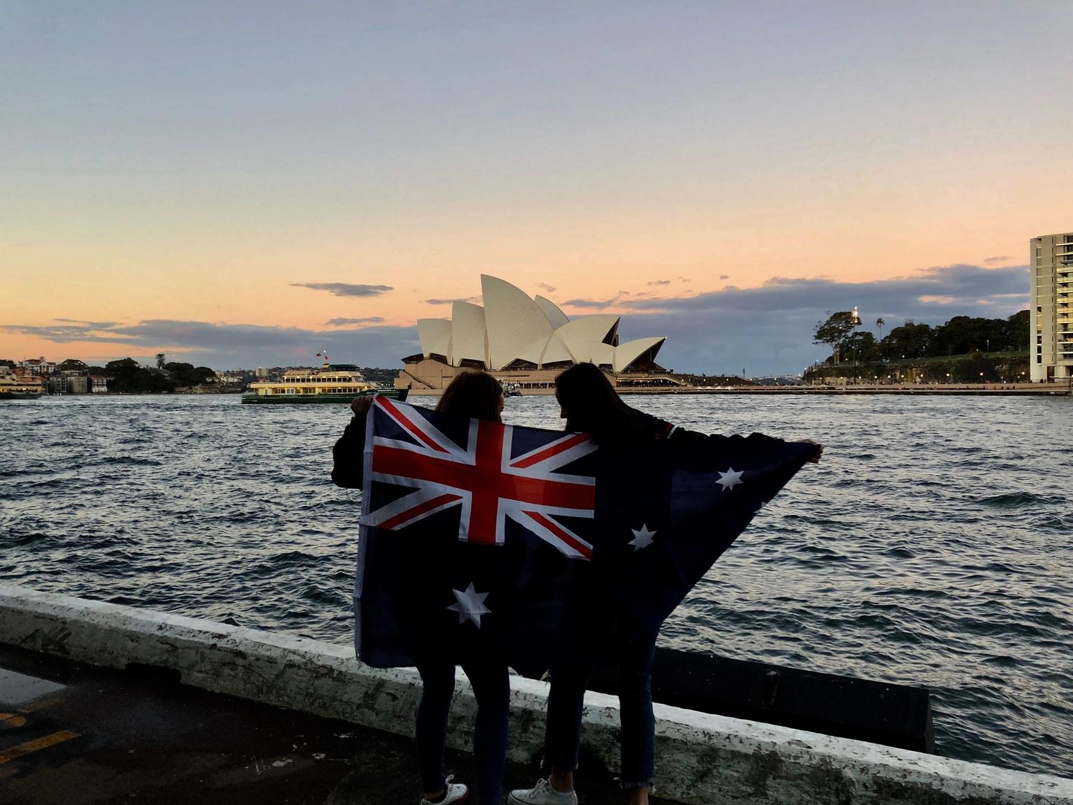 Zwei Menschen mit der Flagge von Australien stehen vor dem Opera Haus in Sydney