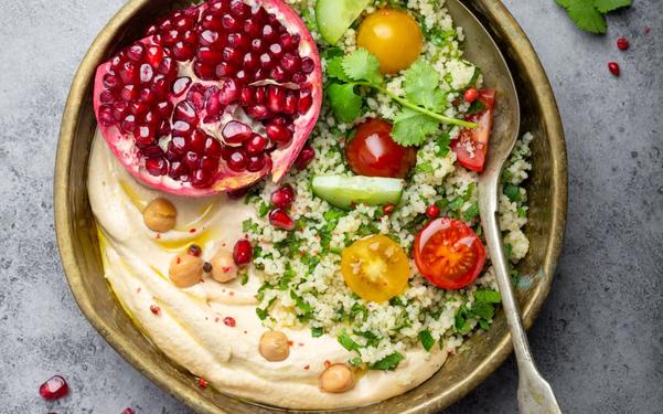 Salade de couscous avec légumes, houmous, grenade et coriandre fraîches