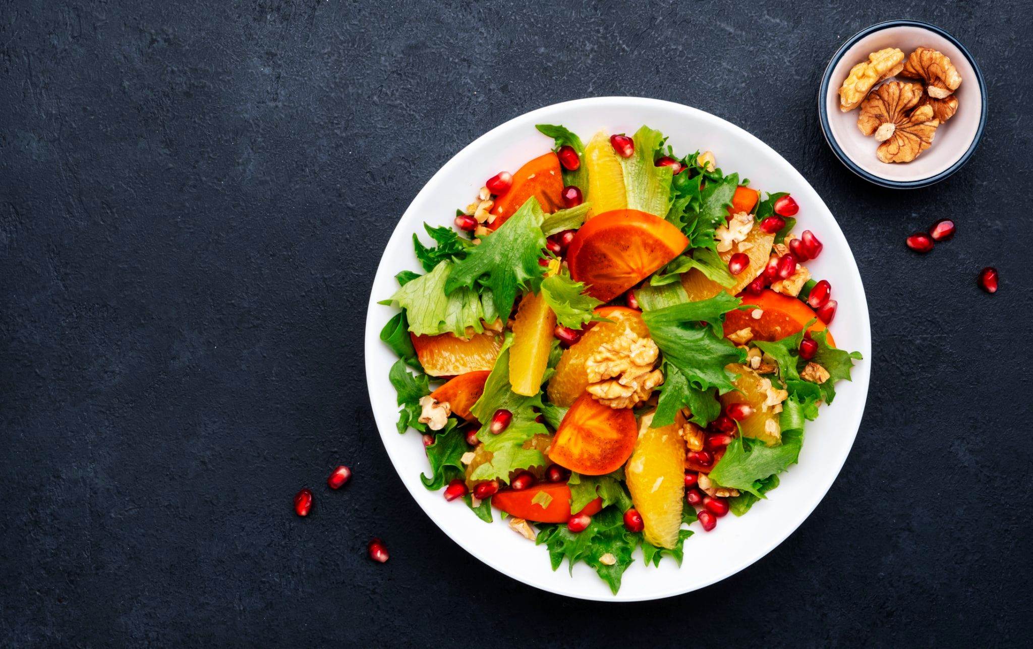 Salade au kaki, aux graines de grenade, noix, tranches d'orange et à la laitue