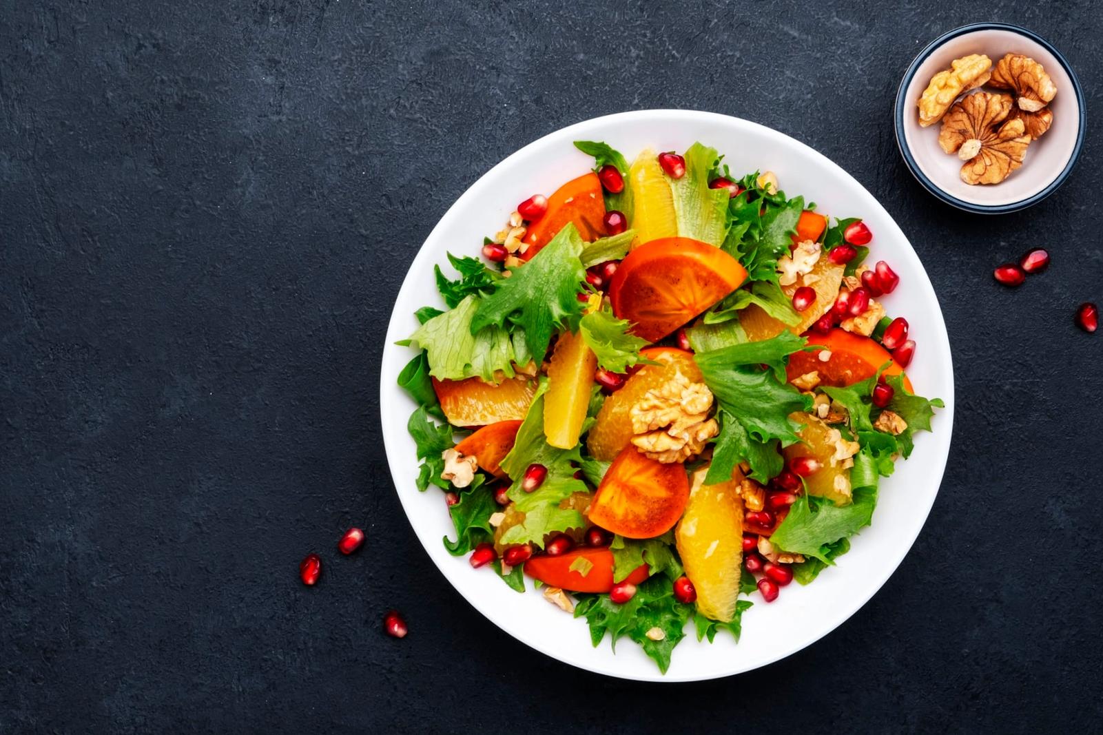Salade au kaki, aux graines de grenade, noix, tranches d'orange et à la laitue