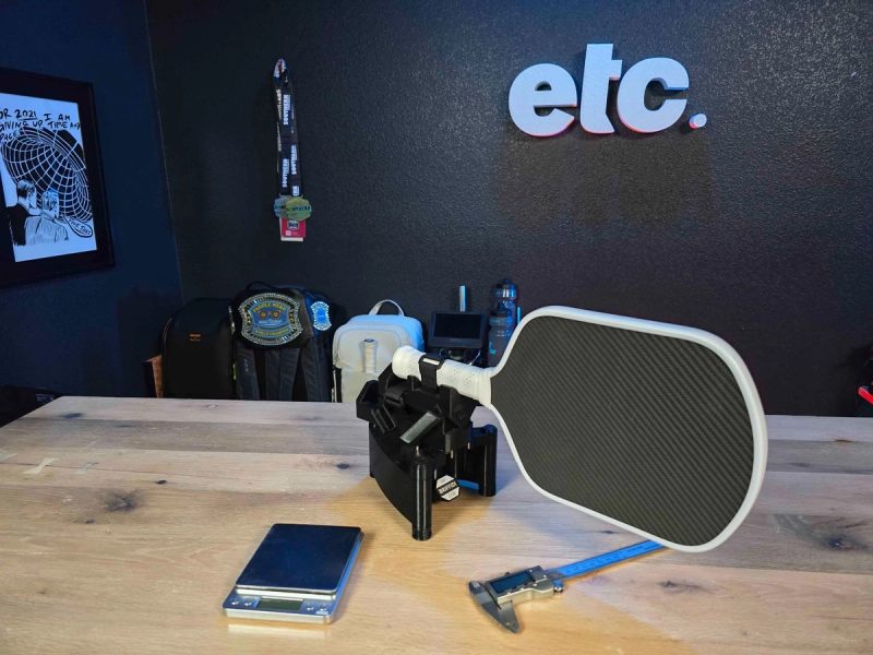 A white-edged carbon paddle propped on a workbench in front of a wall sign reading etc.