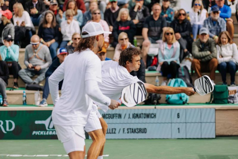 Two players reach for the ball in front of a packed grandstand, the scoreboard reading 6 to 1.