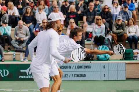 Two players reach for the ball in front of a packed grandstand, the scoreboard reading 6 to 1.