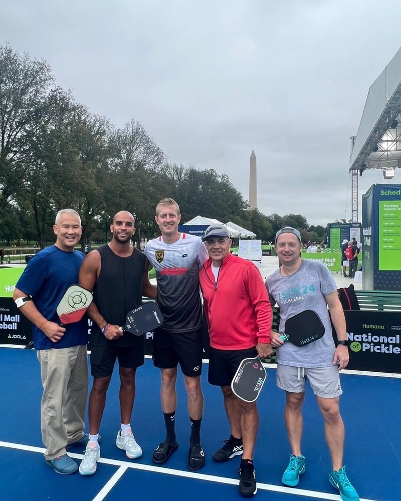 Five men holding paddles pose on a blue court at the National Mall, the Washington Monument behind them.