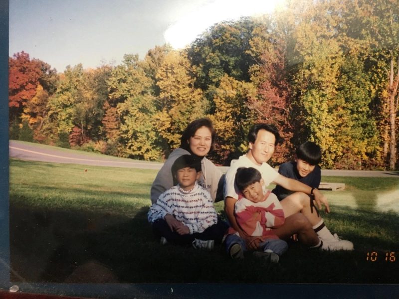 Family photograph of five people sitting on grass in front of autumn trees, dated October 1998.