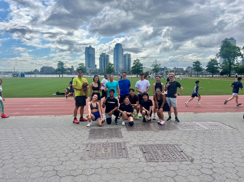 A running group of about fifteen people pose on a waterfront track with a city skyline behind them.