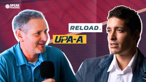 Two men mid-interview, one holding a microphone, with the Reload and UPA-A logos between them.