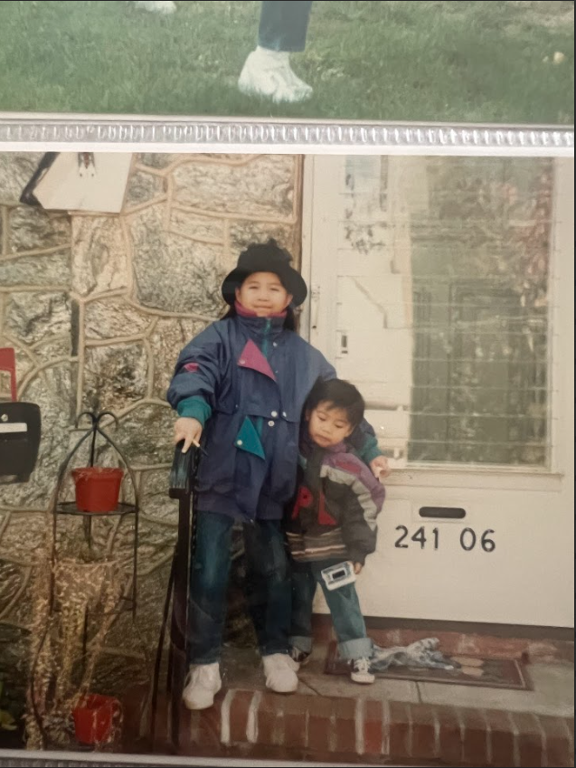 Old photograph of two children in winter coats standing on a front step beside the house number 241 06.