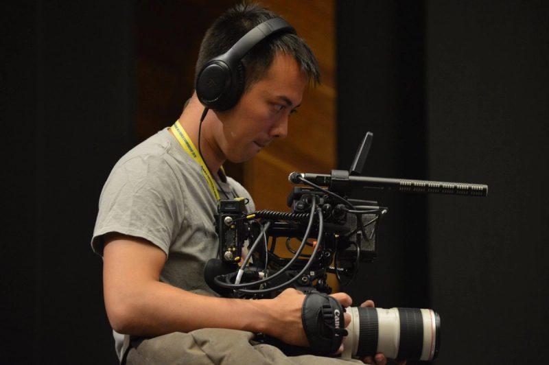 A camera operator in headphones shoulders a rigged cinema camera.