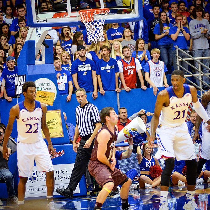 Kansas players in white jerseys under the basket during a packed college basketball game.