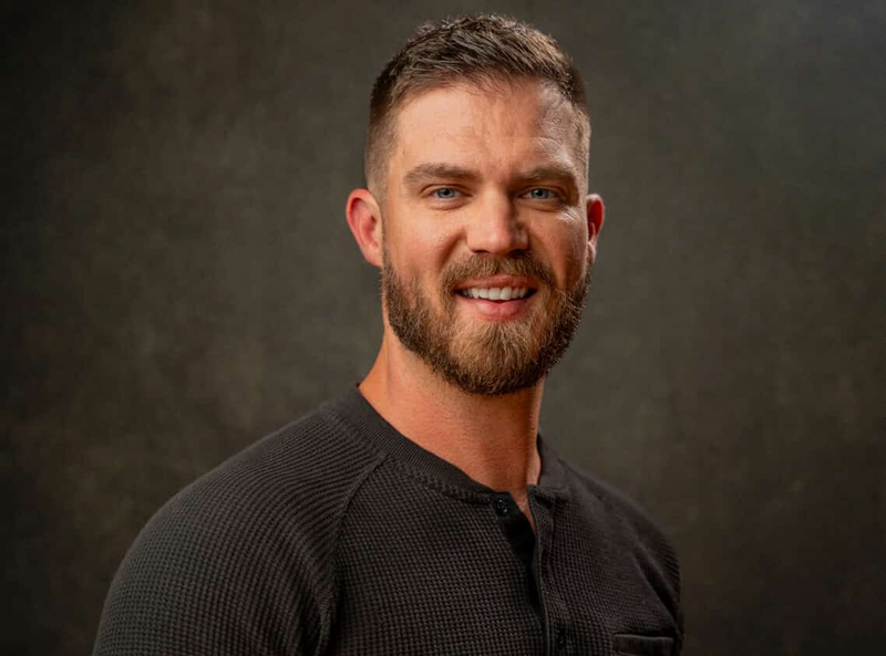 Studio portrait of a smiling bearded man in a dark waffle-knit henley.