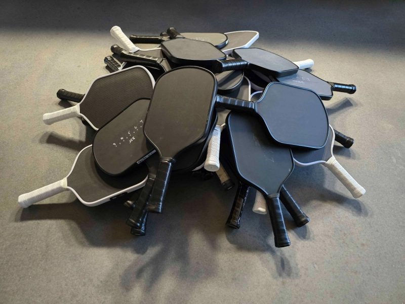 A pile of around twenty unbranded black and white paddles heaped on a grey floor.