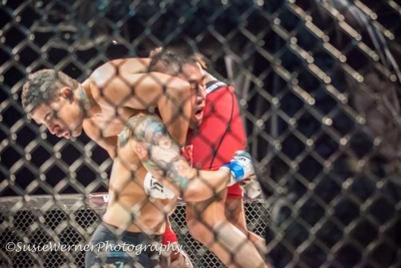 Two fighters grapple against the cage during a mixed martial arts bout.