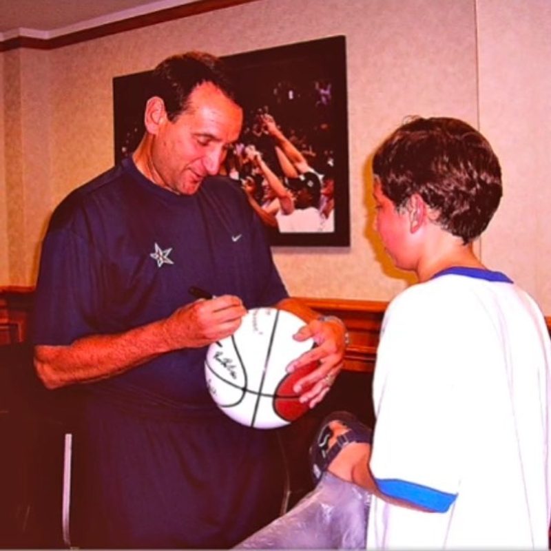 A boy watches a basketball coach sign a ball for him in a hotel lobby.