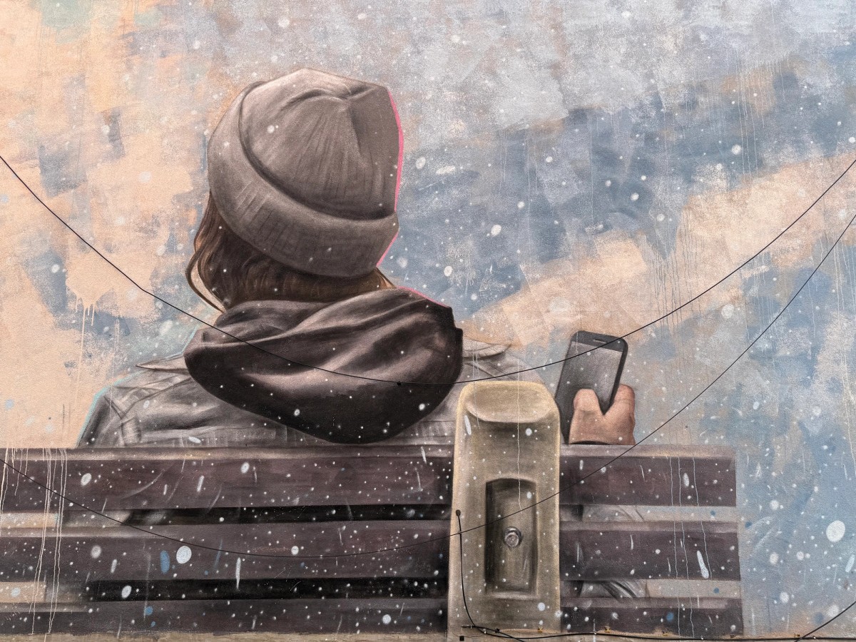 Realistic mural by Ryan Smeeton featuring a person sitting on a bench looking at their phone