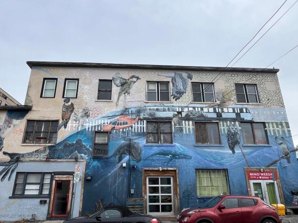 Arpi mural at Railbender Tattoo in Hintonburg featuring giant, realistic hands holding a tattoo gun and a pencil eraser, symbolizing the owner's craft.