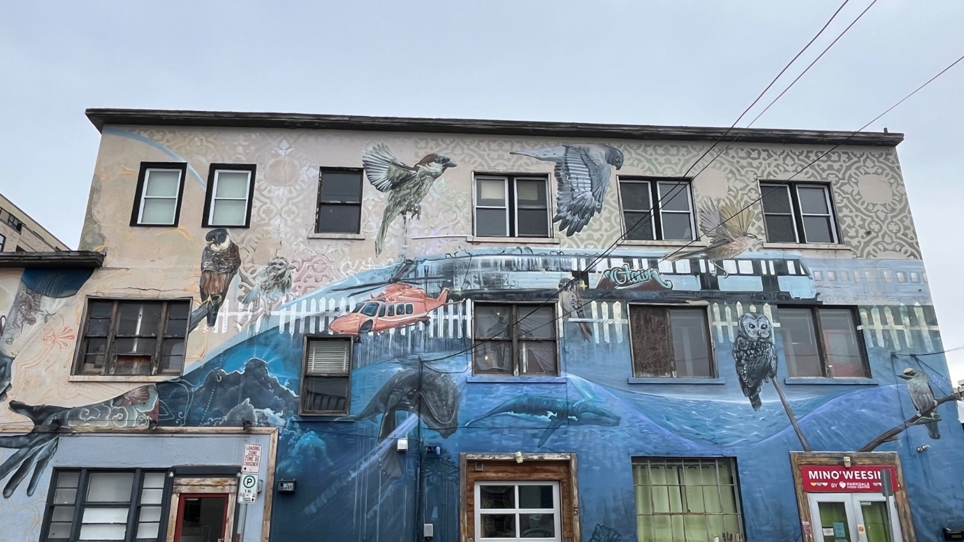 Arpi mural at Railbender Tattoo in Hintonburg featuring giant, realistic hands holding a tattoo gun and a pencil eraser, symbolizing the owner's craft.