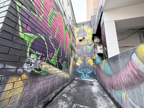 Detailed view of the Graffiti Octobot robot character painting a mural in Ottawa. This Martin Freundorfer street art piece features a mechanical robot interacting with black brick, showcasing the vibrant Ottawa mural artist scene