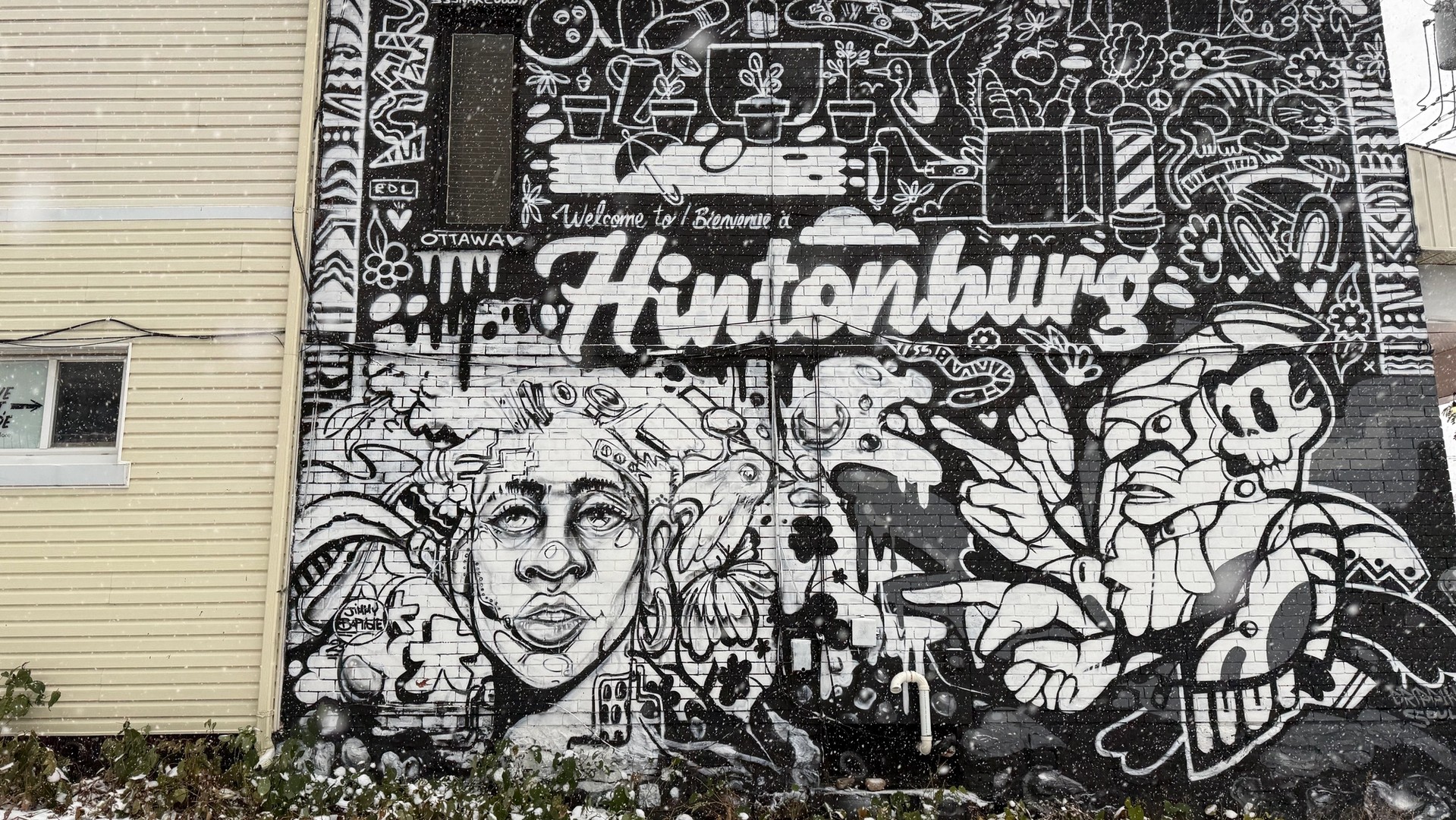 Jimmy Baptiste mural 'Welcome to Hintonburg' rendered in bold black and white graphic style on the brick wall of Urban Art Collective.