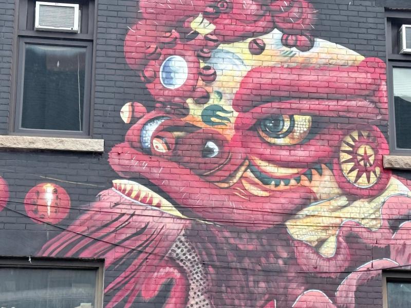 A large red and gold dragon mural painted on a black brick building facade in Ottawa's Chinatown, created by the Higherups.