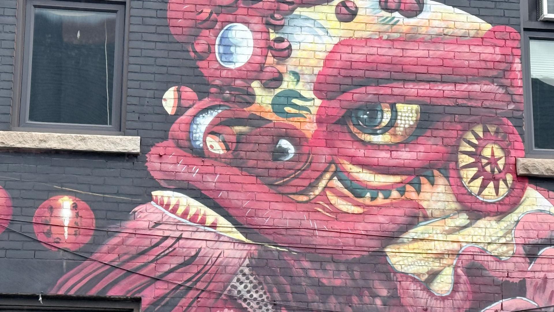 A large red and gold dragon mural painted on a black brick building facade in Ottawa's Chinatown, created by the Higherups.