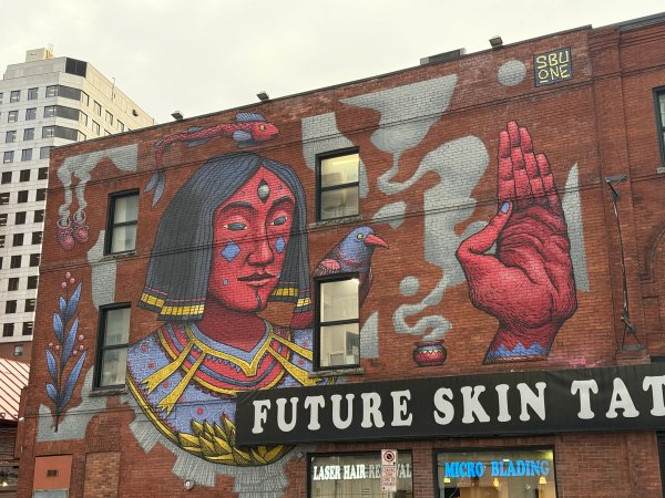 Mural Map Ottawa: Vibrant SbuOne figure with stylized armor and a blue bird. Richly detailed art on a red brick wall in Lowertown.