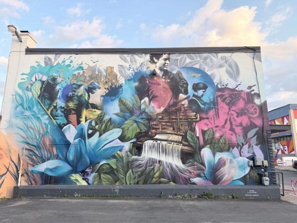Vibrant mural showing laborers, a city, a loom with thread waterfall, and blue flowers, 148 Rue Eddy, Hull, Gatineau, Ottawa.