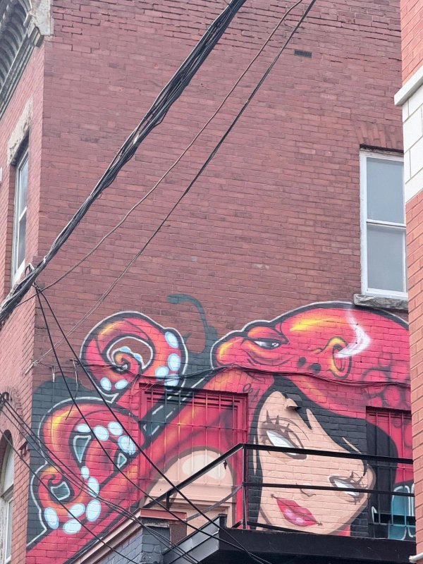 Red, cartoon mural shows octopus and woman on brick, partly hidden by wires and fire escape, 472 Lewis Street, Centretown, Ottawa.