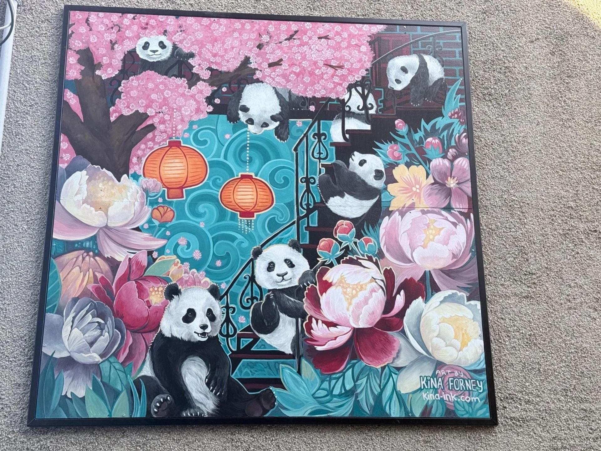 A vibrant mural shows playful pandas among pink cherry blossoms, orange lanterns, and colorful peonies, on Cambridge Street North, Chinatown, Ottawa.