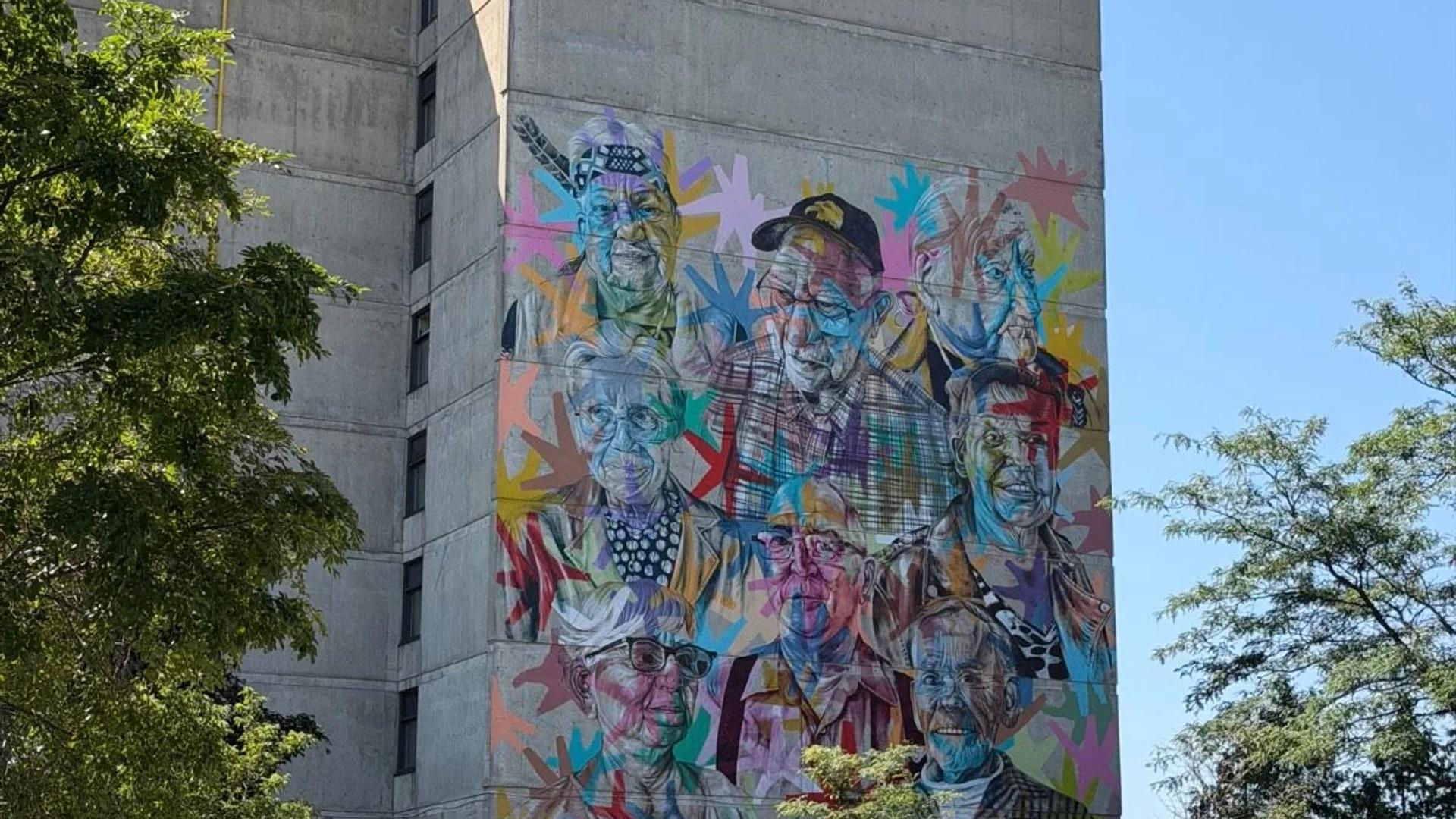 Vibrant pop-art mural of nine portraits on a concrete building, with cars below on Boulevard Sacré-Coeur, Hull, Gatineau, Ottawa.