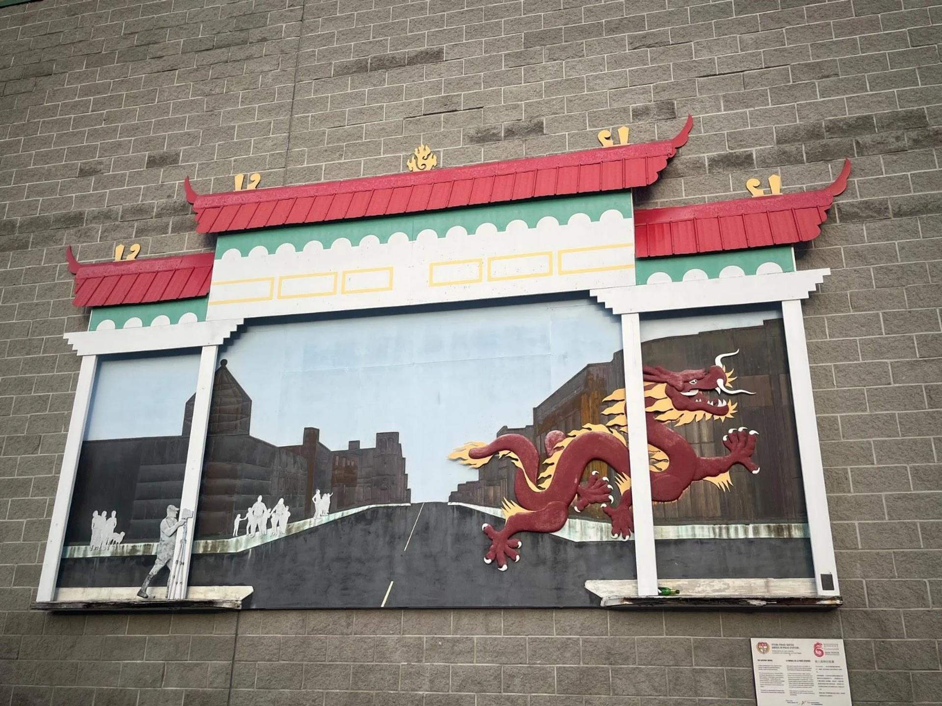 La fresque « The Gateway » de Cairn Cunnane, représentant un dragon courant devant l’arche de Chinatown tandis qu’un policier tient un radar