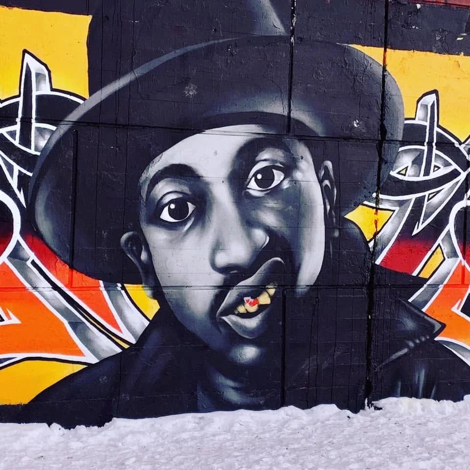 Mural portrait of a grayscale man in a fedora, with a red maple leaf on a gold tooth, against colorful graffiti, Centretown, Ottawa.